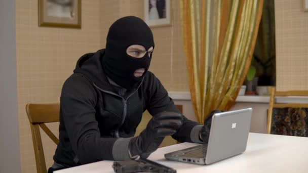 Zloděj se snaží nabourat do laptopu. Maskovaný zločinec sedí v domě a snaží se vloupat do laptopu. Krádež dat z počítače. - Záběry, video