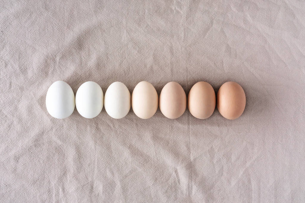 自然のリネンの背景に等しい鶏の卵の行。ウズラの卵、イースターパターンのコレクション. - 写真・画像
