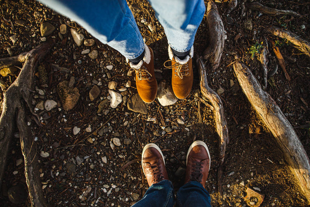 Male and female legs in brown boots in the roots of trees in the sunlight. View from above, flat composition. Family, date, relationship concept - Fotografie, Obrázek