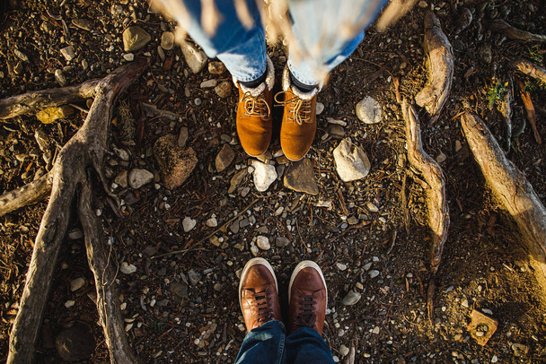 Male and female legs in brown boots in the roots of trees in the sunlight. View from above, flat composition. Family, date, relationship concept - Foto, imagen