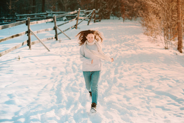 Какая чудесная зима. Веселая молодая женщина бежит по снегу возле леса
. - Фото, изображение