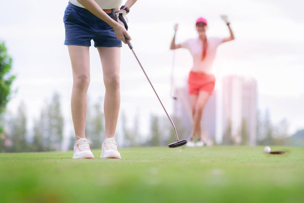 young woman golf player failed to putting golf ball into the hole on the green of the golf course, cheerfully and happiness on the failure of the opponent competitor in background  - 写真・画像