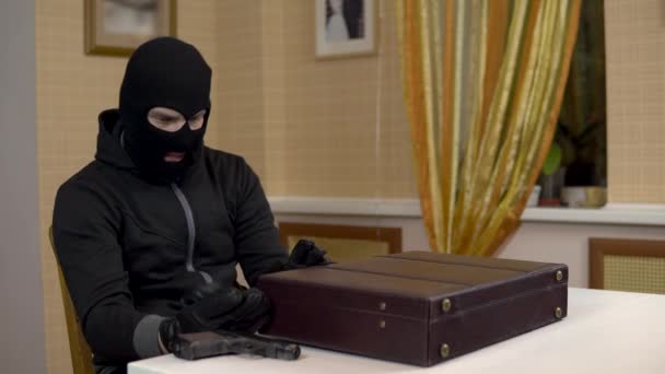 Грабитель пытается открыть чемодан. Бандит в маске открывает чемодан и угрожает пистолетом. Мужчина открыл чемодан и засмеялся.
. - Кадры, видео