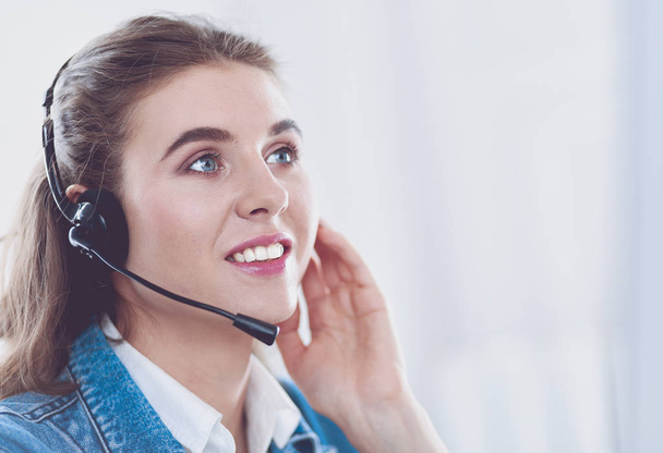 Happy charming young woman sitting and working with laptop using headset in office - Фото, зображення