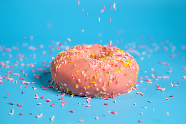 Sprinkles falling from top on Tasty pink strawberry donut. Delicious dessert on blue background. - 写真・画像