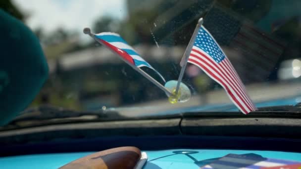 Nahaufnahme von Flaggen Amerikas und Kubas im Auto. Aktion. schöne Fahnen schmücken Panel von Retro-Auto auf dem Hintergrund der Straße in heißen Land. Dekoration für Auto - Filmmaterial, Video
