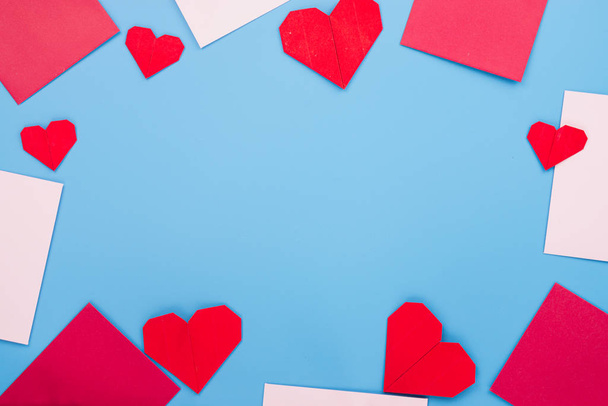 Τα κόκκινα σχήματα καρδιά χαρτί και το φάκελο πάνω από το μπλε φόντο - Φωτογραφία, εικόνα