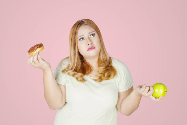 Overweight woman holds donuts and apple fruit - Foto, immagini
