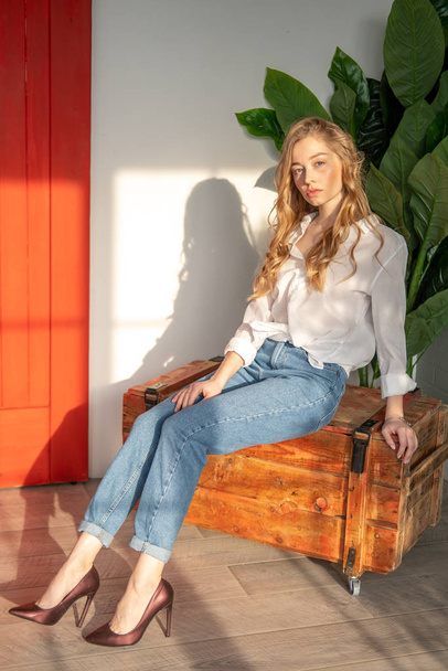 Jovem mulher bonita sentada na caixa de madeira ao lado da planta verde
 - Foto, Imagem