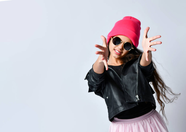 Teenage child in leather jacket, pink hat and sunglasses. She smiling, pulling her hands to you, isolated on white. Close up - Foto, Imagem