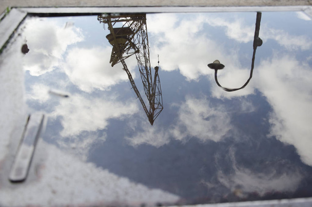 A lighting pole, a crane and a cloudy sky reflected on the surface of the water - Photo, Image
