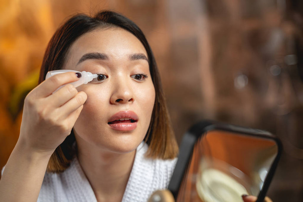 Asian girl is using eye drops indoors - Фото, изображение