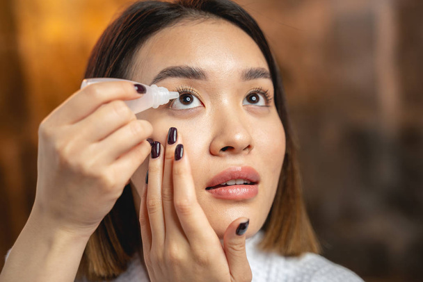 Asian concentrated girl using eye drops indoors - Фото, зображення