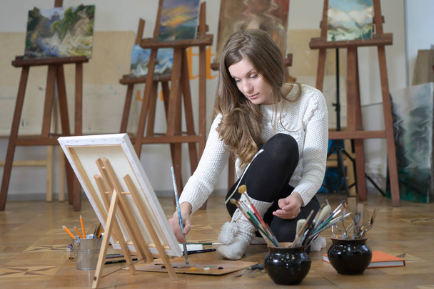 Портрет женщины-художника, сидящей на полу и рисующей в художественной студии
. - Фото, изображение
