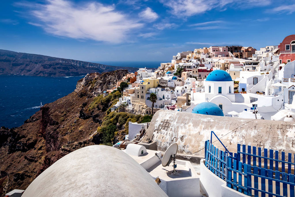 Oia city on Santorini island on a clear sunny day with church on a foreground. Cliff overlooking the sea and the caldera. - Zdjęcie, obraz