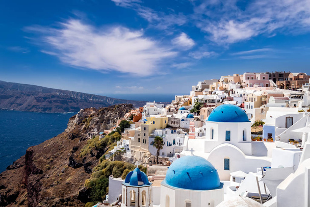 Oia city on Santorini island on a clear sunny day with church on a foreground. Cliff overlooking the sea and the caldera. - Foto, Bild