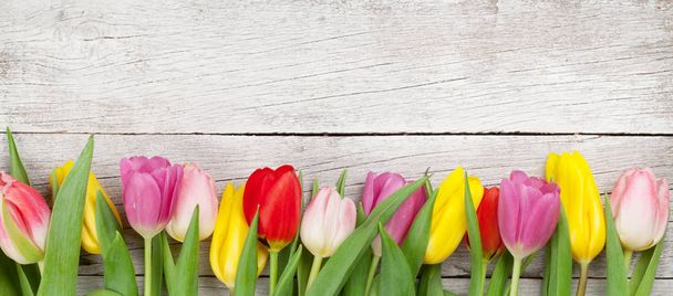 木製の背景に春のチューリップの花とイースターグリーティングカード。コピースペース付きのトップビューフラットレイ - 写真・画像