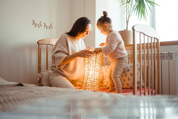 Cheerful mother and her little daughter watching at the lamp. Happy young woman and her little cute daughter enjoy the night light. Happy loving family.  - Фото, изображение