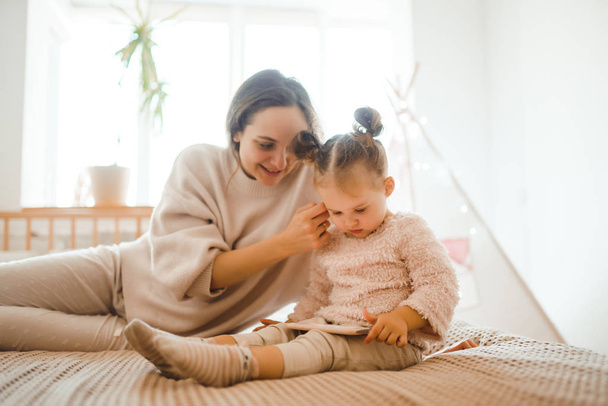 Cheerful mother and her daughter little daughter watching cartoons on phone lying In bed at home. Happy loving family. Modern wireless tech usage free time concept. Bedtime Fun. - Foto, afbeelding