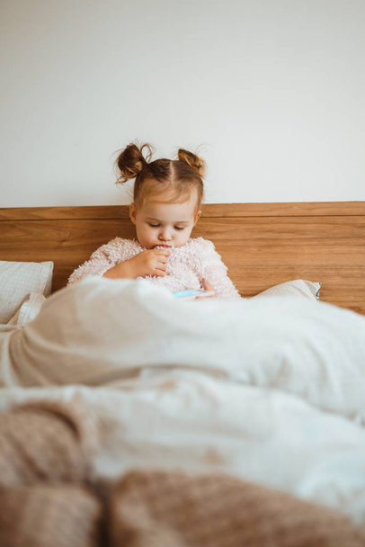 Happy little girl watching cartoons on phone lying In bed at home. Happy loving family. Modern wireless tech usage free time concept. Bedtime Fun. - Foto, Imagem