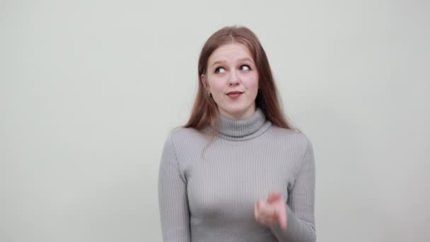 Ένα κορίτσι της ευρωπαϊκής εμφάνισης δείχνει γλώσσα γκρι φόντο. - Πλάνα, βίντεο