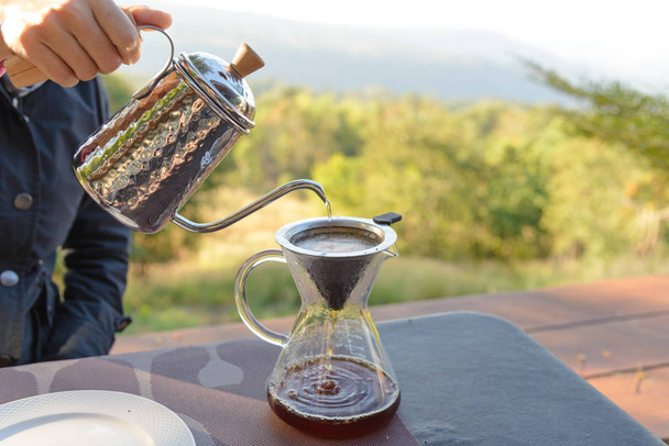 Hand druppelkoffie maken giet over koffie met warm water wordt gegoten uit een waterkoker met uitzicht op de bergen en natuurlijk groen uitzicht gevoel chill en ontspannen in de natuur - Foto, afbeelding