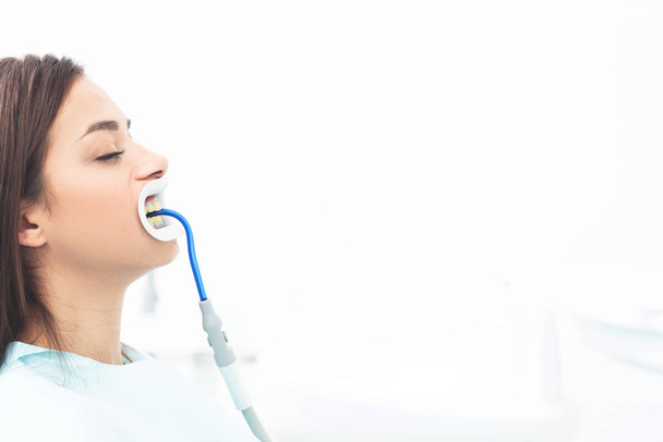 Big cover image with space for text. On left side young female patient sitting in dental clinic after teeth whitening. In mouth she hold an instrument for aspiration - Fotoğraf, Görsel