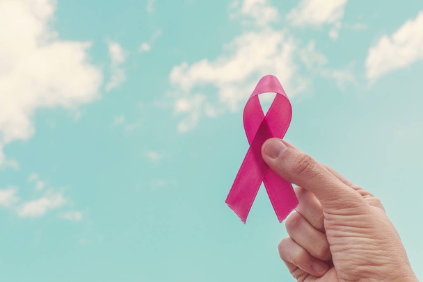 Hand hält rosa Schleife über blauem Himmel, Weltkrebstag, Brust - Foto, Bild