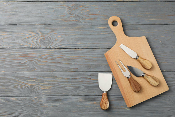Board and cheese knives on wooden background, top view and space - Valokuva, kuva