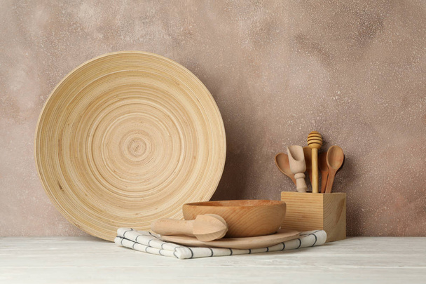 Wooden tableware and cutlery on white table against brown backgr - Fotografie, Obrázek