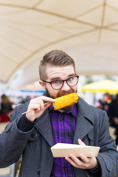 Vegetariano y concepto de comida - Hombre guapo comiendo maíz en la calle en el festival de comida rápida
 - Foto, imagen