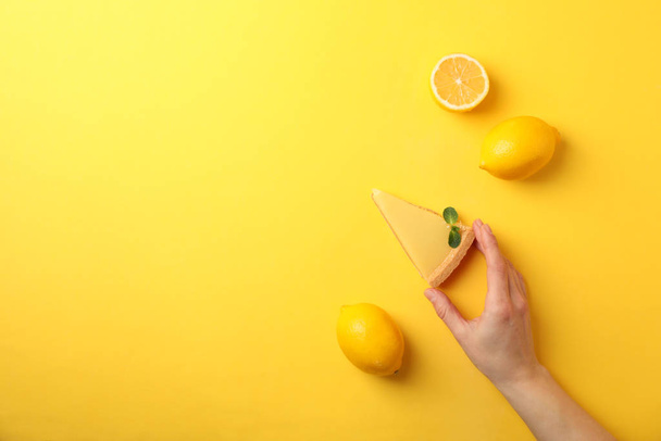 Person hold slice of lemon tart on yellow background, top view - Photo, Image