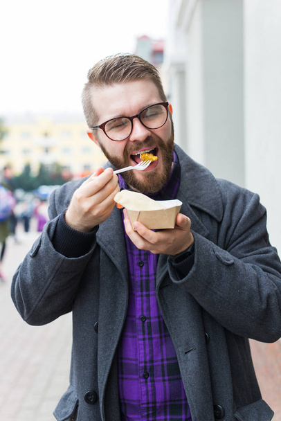 Junk food, eating and lifestyle concept - young man with meal eats on city street. - Photo, Image
