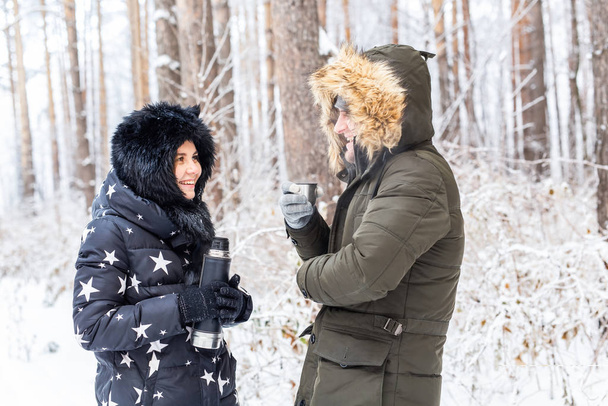 Εποχή και περπάτημα έννοια - Ευτυχισμένο ζευγάρι πίνοντας ζεστό τσάι στο δάσος του χειμώνα - Φωτογραφία, εικόνα