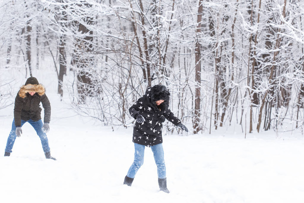 Lifestyle, season and leisure concept - Funny couple playing snowball in winter park - 写真・画像