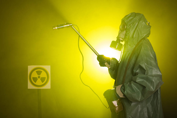 Radyasyon, kirlilik ve tehlike kavramı - koruyucu giysiler içinde bir adam ve karanlık arka planda bir gaz maskesi - Fotoğraf, Görsel