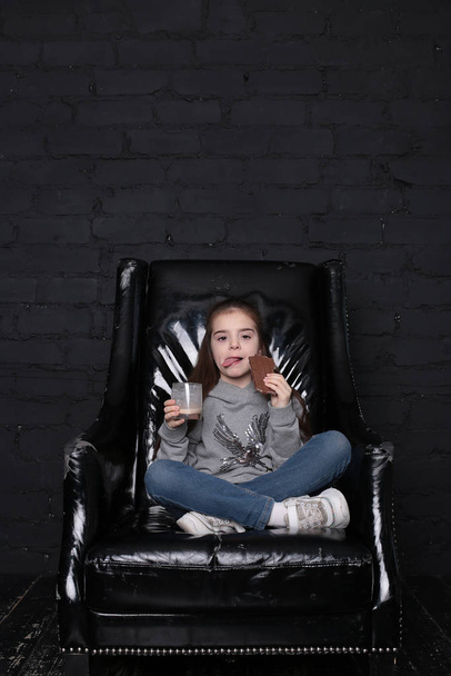 дівчина з довгим волоссям у сірому светрі у великому чорному кріслі в інтер'єрі лофт
 - Фото, зображення
