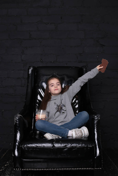 girl with long hair in a gray hoodie in a large black armchair in the loft interior - Photo, Image