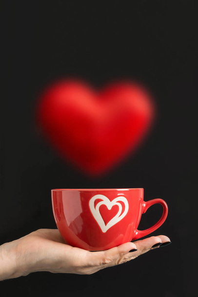 Valentine's Day card. Woman holding red cup of coffee with flying heart isolated on black. Concept. - Photo, Image