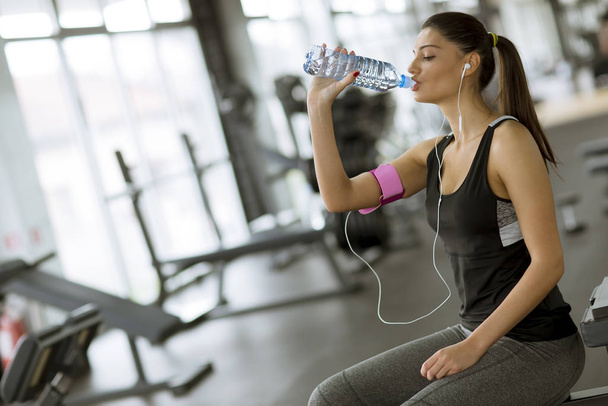 Vonzó sport fiatal nő ivóvíz, miközben ül és pihen edzés után a tornateremben - Fotó, kép
