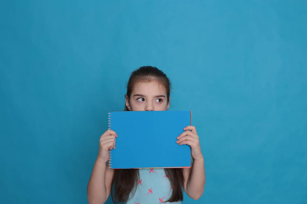 Sekiz yaşında neşeli, sevgi dolu bir kız ve mavi arka planda kayıt için renkli bir sayfa dolusu boş alan. - Fotoğraf, Görsel