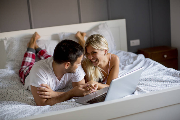 Интимные молодые любовники используют ноутбук, лежа на кровати в спальне
 - Фото, изображение