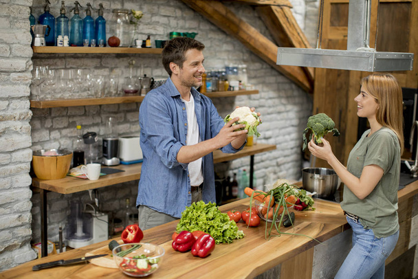Trendy young couple peeling and cutting vegetables from the market in rustic kitchen - 写真・画像