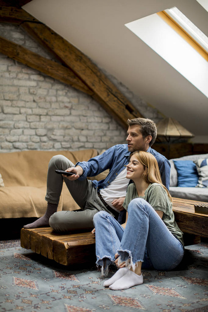 Smiling lovely young couple relaxing and watching TV at rustic home - 写真・画像