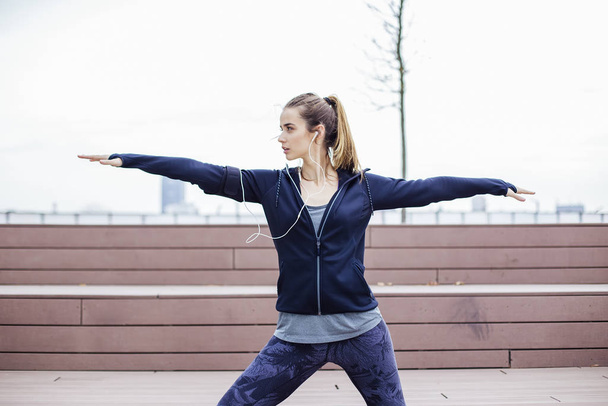 Mooie jonge vrouw met koptelefoon stretching tijdens sport training in de stedelijke omgeving - Foto, afbeelding