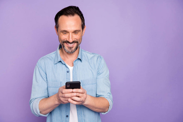 Portrait of positive cheerful man use smart phone chatting blog post follow bloggers share social media information wear good looking clothing isolated over violet color background - Foto, Imagem