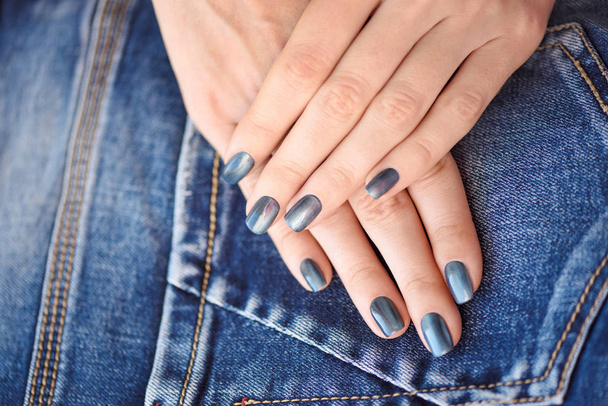 Manos con uñas manicura azul oscuro sobre fondo textil jeans
 - Foto, imagen