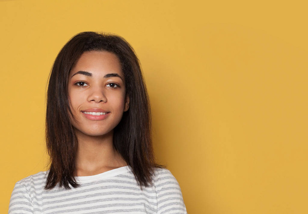 Mooie Afro-Amerikaanse vrouw student glimlachen op gele achtergrond - Foto, afbeelding