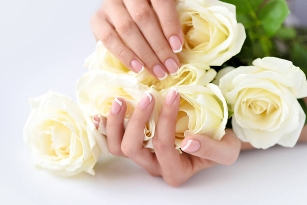 Handen van een vrouw met mooie franse manicure en witte rozen - Foto, afbeelding