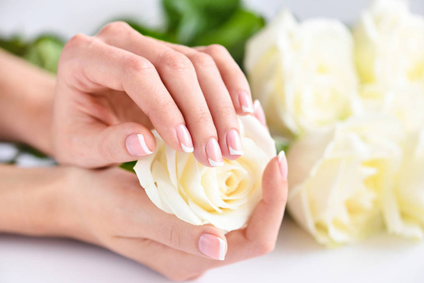 Ręce kobiety z pięknym francuskim manicure i białe róże - Zdjęcie, obraz